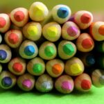 Buntstifte sind aufeinander gestapelt, mit sichtbaren Spitzen in verschiedenen Farben, auf einer grünen Oberfläche und verschwommenem Hintergrund.